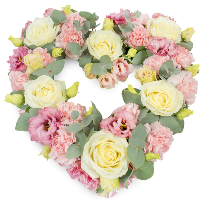 Set against a stark white background, a beautifully detailed heart-shaped floral wreath takes centre stage, its form clearly defined and completely filled with soft, romantic blooms. Larger cream and pale yellow roses provide structure, spaced evenly around the curve of the heart so their velvety petals and spiralled centres become natural focal points. Between these roses, clusters of pastel pink carnations are nestled tightly together, their fringed petals creating a plush, textured surface that softens every edge. Deeper pink and mauve lisianthus flowers appear thoughtfully throughout, some with fully opened, cupped petals, others still in bud, the varied stages adding a sense of life and gentle progression. Woven organically through the flowers, stems of eucalyptus with round, silvery-green leaves bring in a cool, calming shade that balances the warmer creams and pinks, and subtly outlines the heart's graceful contour. Here and there, small yellow-green buds break through the petals, signalling freshness and the careful handwork of an experienced local florist who understands the importance of every detail when preparing sympathy flowers for families around Seven Sisters. The overall composition feels dense yet breathable, with just enough space between blooms to appreciate each texture and hue. Imagining this piece in real life, you can almost feel the softness of the petals and catch a whisper of floral fragrance mingling with the light, woody scent of eucalyptus. This heart wreath would make a moving focal tribute at a funeral service, graveside committal, or memorial gathering in Seven Sisters, symbolising tenderness, gratitude, and enduring affection for someone deeply missed.